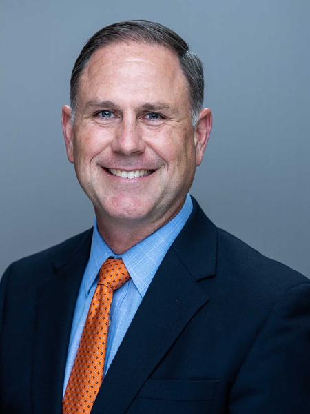 Dan Cook portrait, smiling in blue suit and burnt orange tie